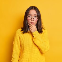 woman in glasses holding her chin looking confused