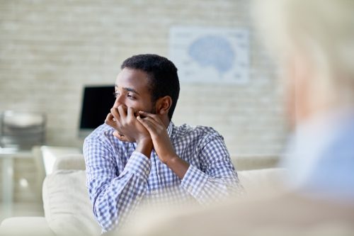 man sitting on sofa in psychotherapy office and looking away deep in thought