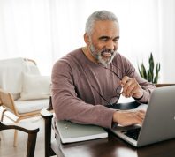 A senior man checking his laptop at home while smiling