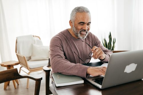 A senior man checking his laptop at home while smiling