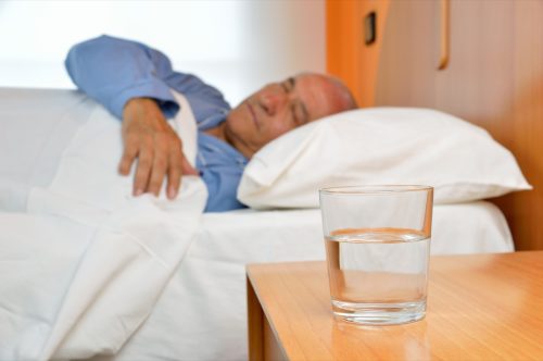 Senior man lying on bed with glass of water on the nightstand