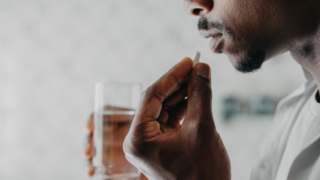 A closeup of a person taking a pill capsule with a glass of water in their other hand