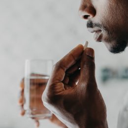 A closeup of a person taking a pill capsule with a glass of water in their other hand