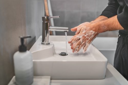Washing hands with soap and hot water at home bathroom sink man cleansing hand hygiene