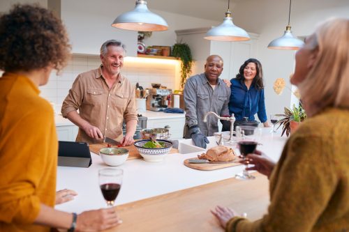 Group Of Mature Friends Meeting At Home Preparing Meal And Drinking Wine Together