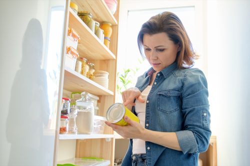 Woman in pantry with groceries, wooden rack for storing food in the kitchen.