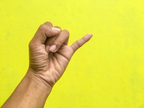 man holding up his pinkie finger in front of a yellow background