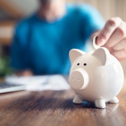 Close up of a person putting a coin into a white piggy bank