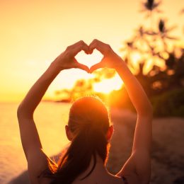 woman making a heart shape with her hands at sunset