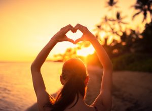 woman making a heart shape with her hands at sunset