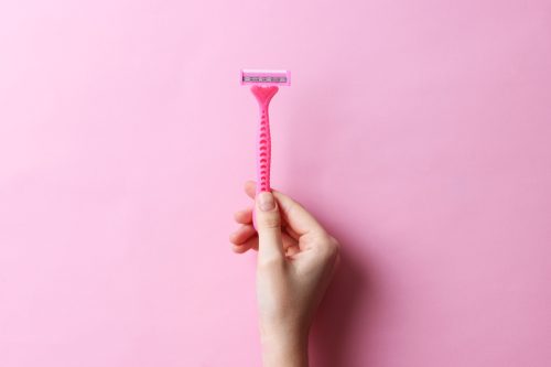 woman holding up pink razor in front of pink background