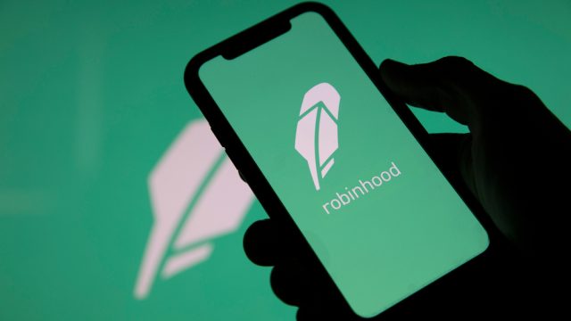 A closeup of a hand holding a phone with the Robinhood stock trading app logo on the screen