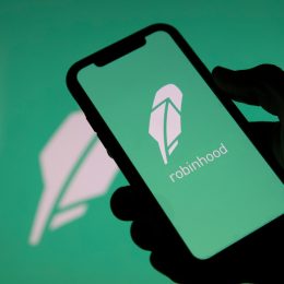 A closeup of a hand holding a phone with the Robinhood stock trading app logo on the screen