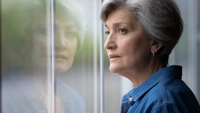 A sad, regretful-looking woman with short gray hair looking out the window