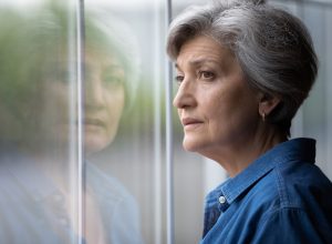 A sad, regretful-looking woman with short gray hair looking out the window
