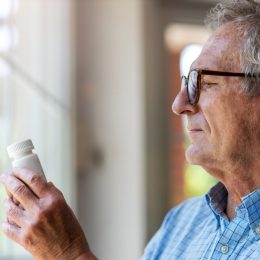 A senior man looking at a supplement bottle while standing near a window