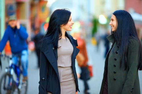 two woman smiling and talking on the street