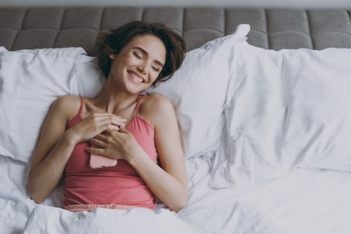 woman laying in bed holding her phone and smiling after receiving a sweet good morning message from her boyfriend