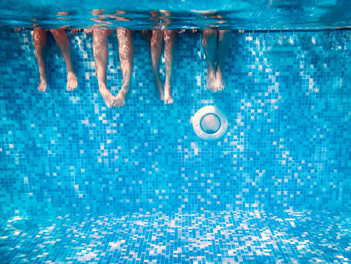 Bàn chân của trẻ em và người lớn dưới nước trong bể bơi