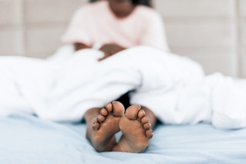 black woman in bed sticking her bare feet out of the covers