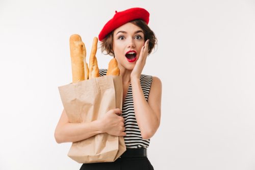 Portrait of a surprised woman wearing beret holding paper bag with a baguette