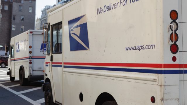 Three US Postal Service delivery vans are parked beside the Canal Street Station on Church Street in Downtown Manhattan. The USPS uses these Grumman vans to collect and deliver bags of mail and packages to local drop off areas and to sorting offices. The eagles head logo printed on the rear of these trucks is a current advertising trademark used by the USPS. The USPS web site URL is printed on the side of the van. Red, white, and blue are the colors used by the USPS in their advertising.