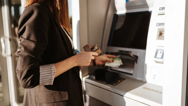 Young woman using outdoor cash machine on sunny spring day