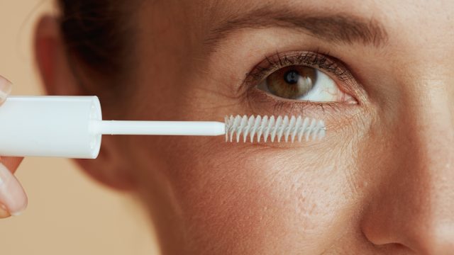 Close up of a woman applying a clear mascara gel in a white tube to her eyelashes