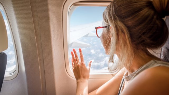 Young,Woman,Enjoying,The,View,Through,The,Aircraft,Window,Sitting