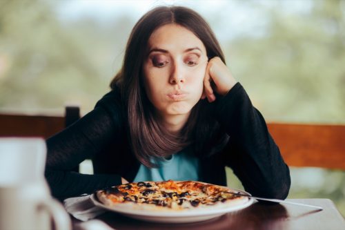 Sad Woman Looking at the Pizza in Her Plate. Female obsessing over counting calories thinking about eating fast-food