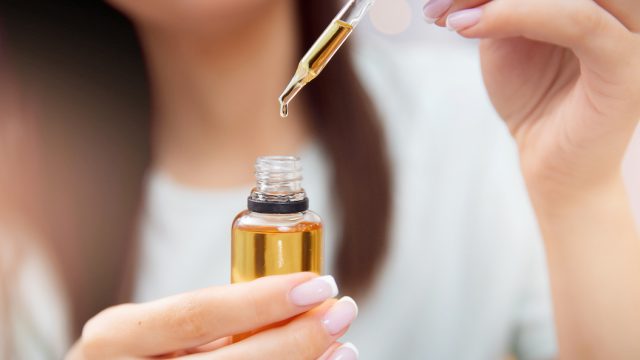 Blurred close up of a woman holding a castor oil dropper