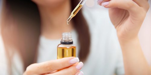 Blurred close up of a woman holding a castor oil dropper
