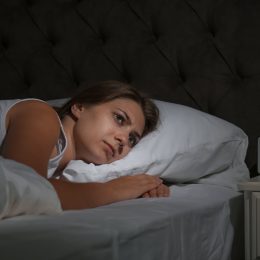 Woman lying awake in bed in the middle of the night looking scared.