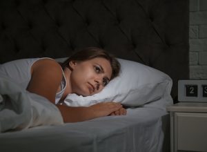 Woman lying awake in bed in the middle of the night looking scared.
