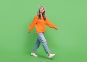 Full body photo of woman with gray hair wearing slouchy boyfriend jeans and sneakers isolated on green color background