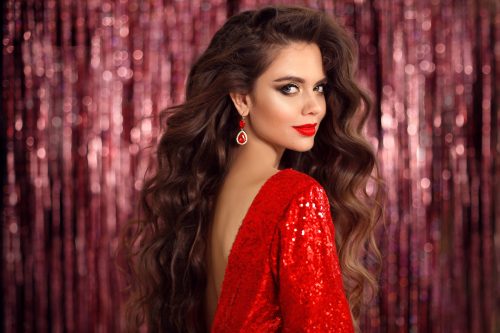 A beautiful brunette woman wearing a backless red sequin dress with matching red lips and ruby earrings
