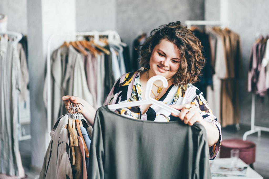 A smiling woman shops in a store for plus size clothing