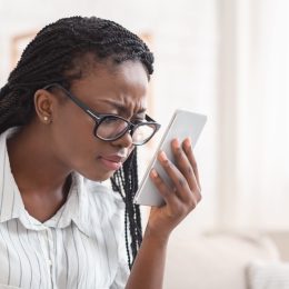 young black woman wearing glasses and squinting at her phone