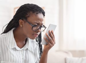 young black woman wearing glasses and squinting at her phone