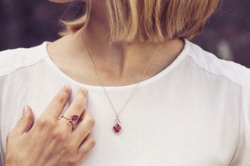Close up of a blonde woman wearing a garnet necklace and ring against a white shirt
