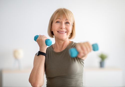 Strong senior woman doing exercises with dumbbells indoors.