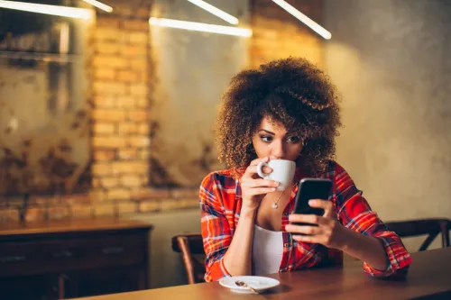 Woman Drinking Coffee While on Her Phone