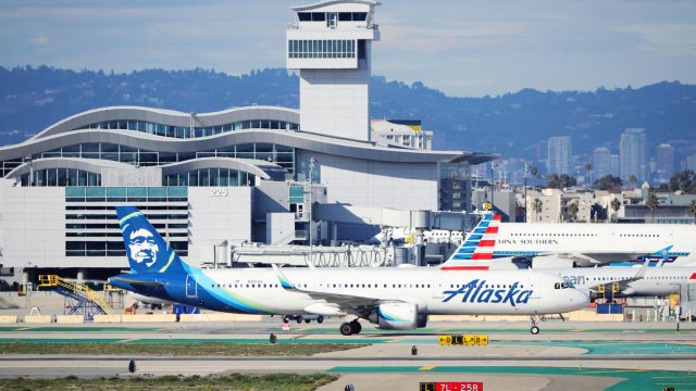 An Alaska Airlines plane on a busy runway in front of an American Airlines jet