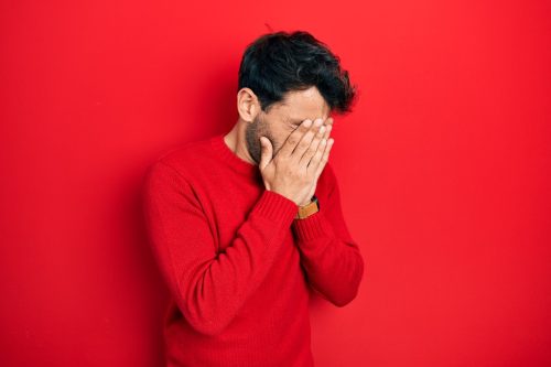 man covering his face across a red background