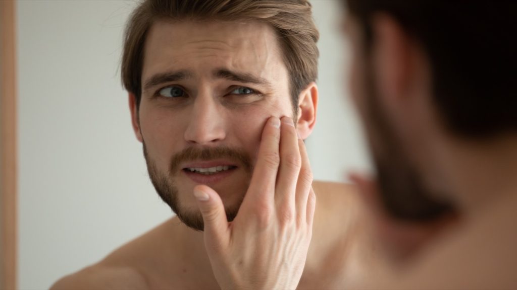 insecure man examines his skin in the mirror