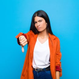 woman looking angry giving the "thumbs down" sign over a blue background