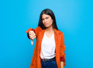 woman looking angry giving the "thumbs down" sign over a blue background