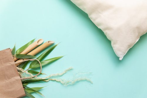 Flat lay of eco friendly materials. Zero waste still life with bamboo leaves in bag, bamboo pillow over green background.