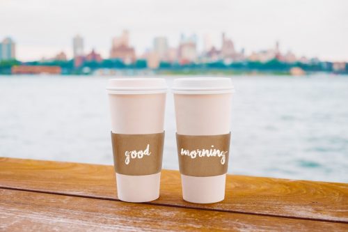 a good morning message appears on two cups of coffee overlooking the New York City skyline