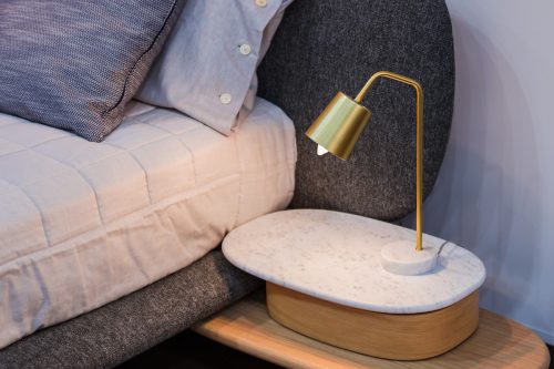 Brass lamp on bedside table against lavender walls and bedding.